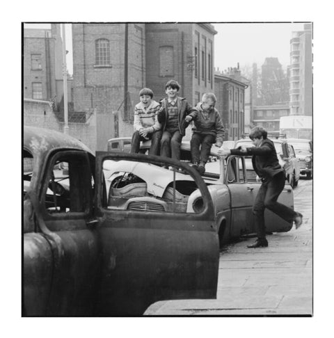 Four boys play on wrecked cars parked in the street 1967