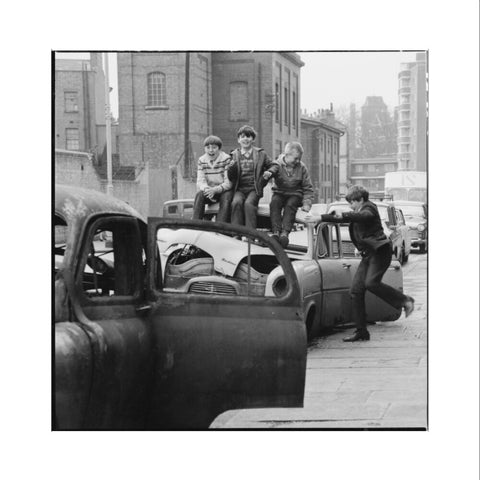 Four boys play on wrecked cars parked in the street 1967