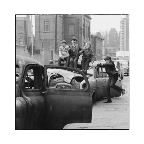 Four boys play on wrecked cars parked in the street 1967