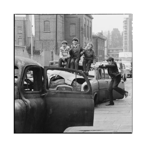 Four boys play on wrecked cars parked in the street 1967