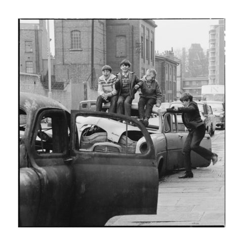 Four boys play on wrecked cars parked in the street 1967