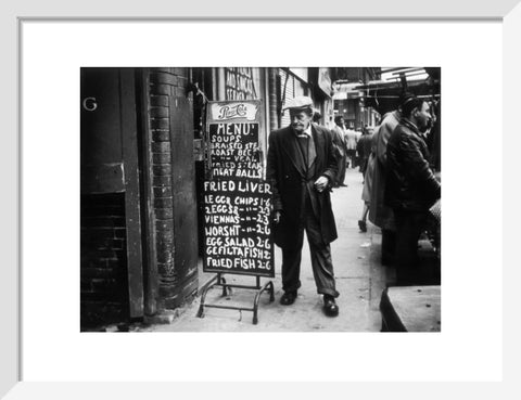 A man reads a chalk board on the street outside a cafe1961