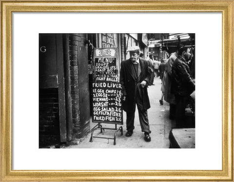 A man reads a chalk board on the street outside a cafe1961