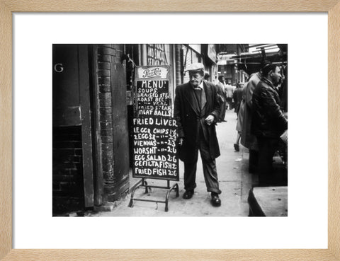 A man reads a chalk board on the street outside a cafe1961