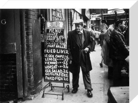 A man reads a chalk board on the street outside a cafe1961