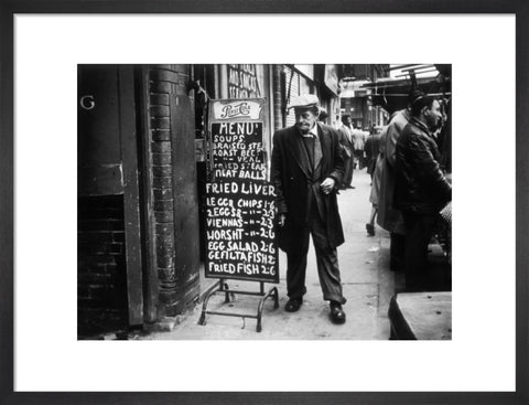 A man reads a chalk board on the street outside a cafe1961