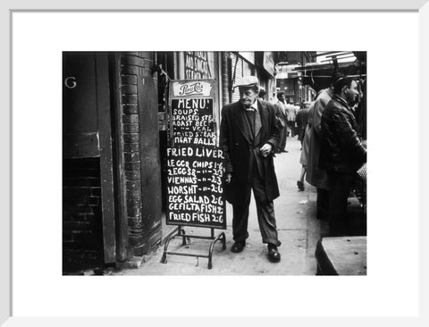 A man reads a chalk board on the street outside a cafe1961