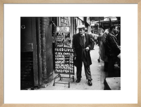 A man reads a chalk board on the street outside a cafe1961