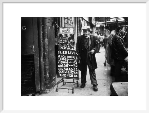 A man reads a chalk board on the street outside a cafe1961