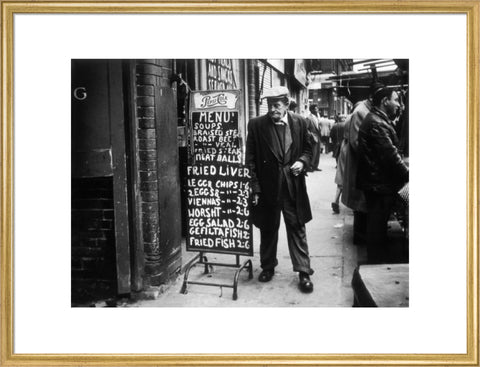 A man reads a chalk board on the street outside a cafe1961