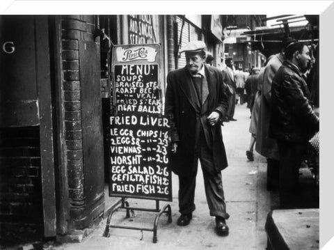 A man reads a chalk board on the street outside a cafe1961