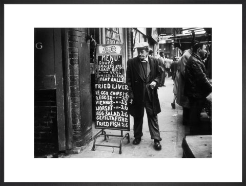 A man reads a chalk board on the street outside a cafe1961