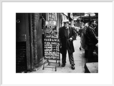 A man reads a chalk board on the street outside a cafe1961