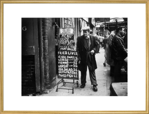 A man reads a chalk board on the street outside a cafe1961