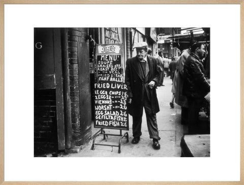 A man reads a chalk board on the street outside a cafe1961