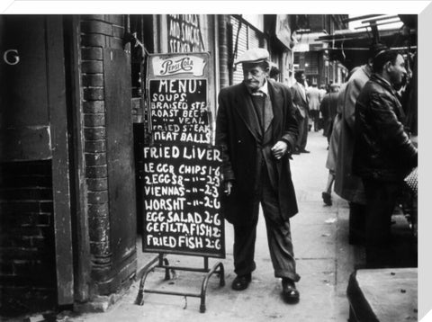 A man reads a chalk board on the street outside a cafe1961