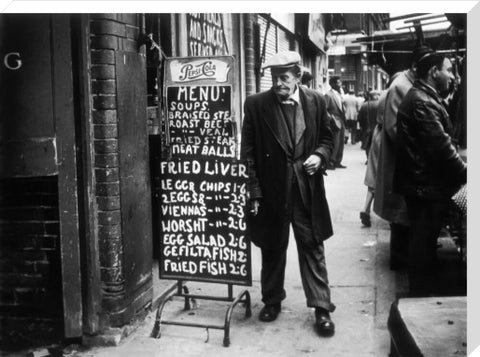 A man reads a chalk board on the street outside a cafe1961