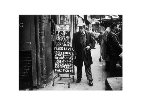 A man reads a chalk board on the street outside a cafe1961