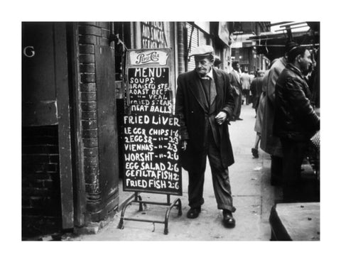 A man reads a chalk board on the street outside a cafe1961