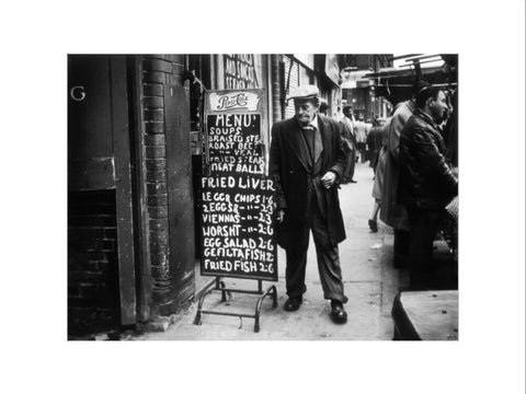 A man reads a chalk board on the street outside a cafe1961