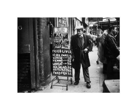 A man reads a chalk board on the street outside a cafe1961