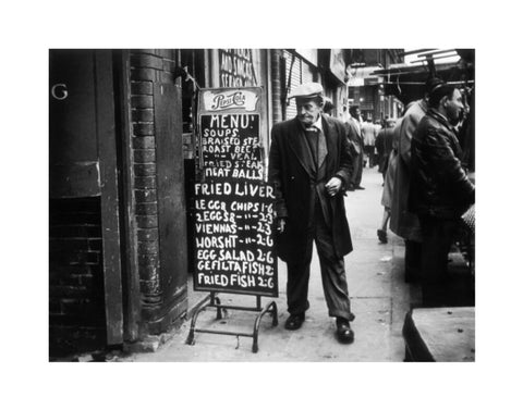 A man reads a chalk board on the street outside a cafe1961