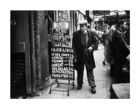 A man reads a chalk board on the street outside a cafe1961