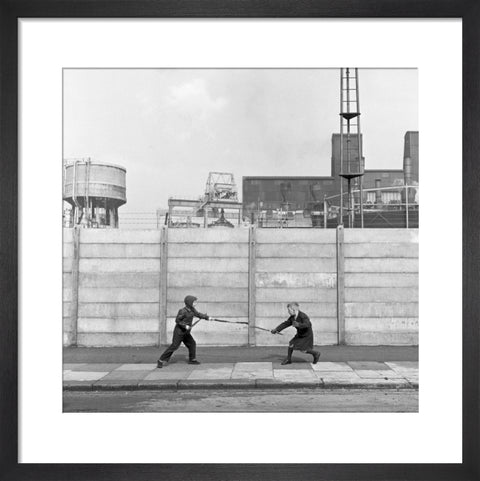 Two boys fighting with sticks in front of a concrete wall. c.1955