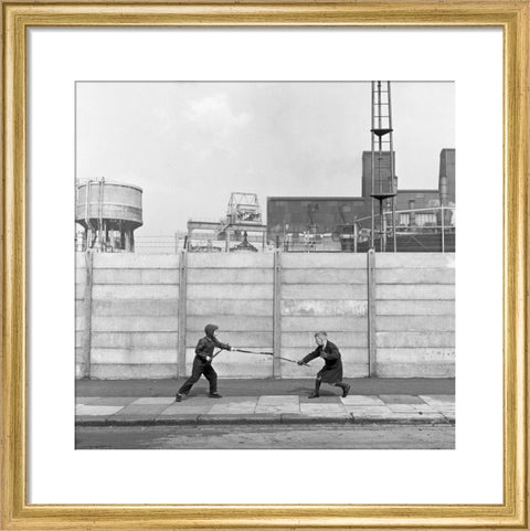 Two boys fighting with sticks in front of a concrete wall. c.1955