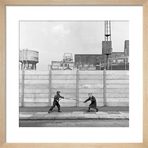 Two boys fighting with sticks in front of a concrete wall. c.1955