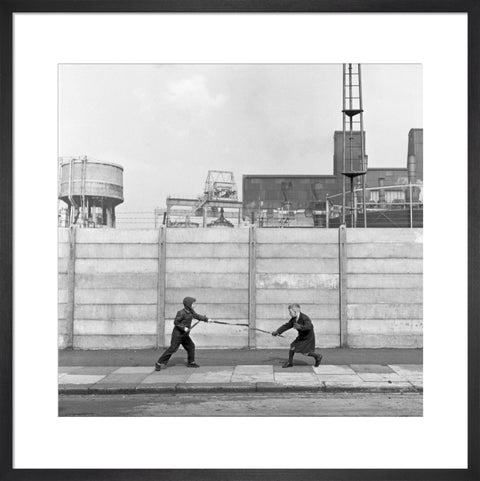 Two boys fighting with sticks in front of a concrete wall. c.1955