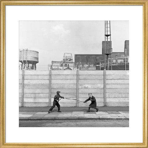 Two boys fighting with sticks in front of a concrete wall. c.1955