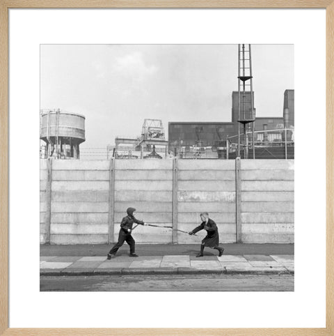 Two boys fighting with sticks in front of a concrete wall. c.1955