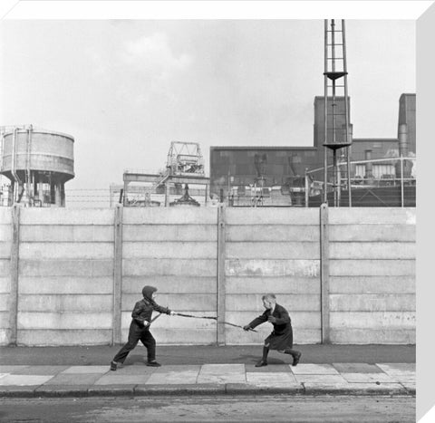 Two boys fighting with sticks in front of a concrete wall. c.1955