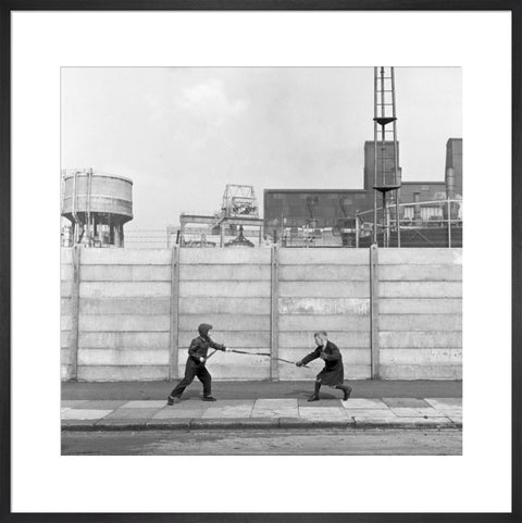 Two boys fighting with sticks in front of a concrete wall. c.1955