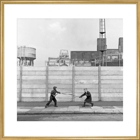 Two boys fighting with sticks in front of a concrete wall. c.1955