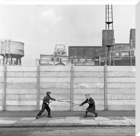 Two boys fighting with sticks in front of a concrete wall. c.1955