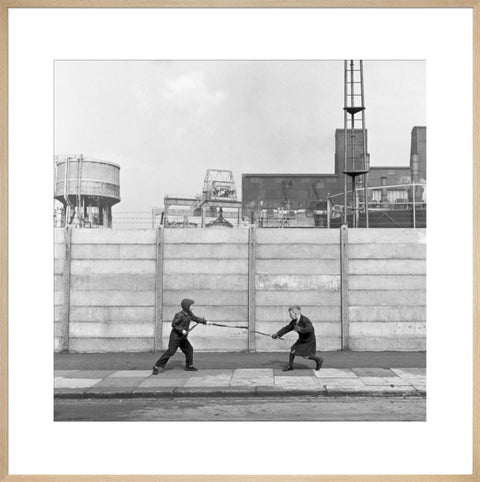 Two boys fighting with sticks in front of a concrete wall. c.1955