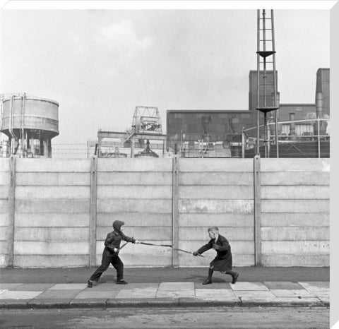 Two boys fighting with sticks in front of a concrete wall. c.1955