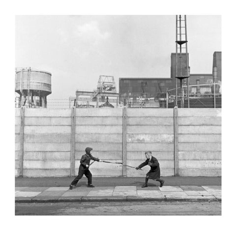 Two boys fighting with sticks in front of a concrete wall. c.1955