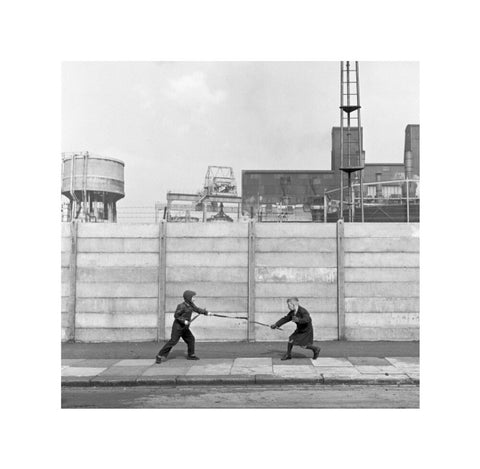 Two boys fighting with sticks in front of a concrete wall. c.1955