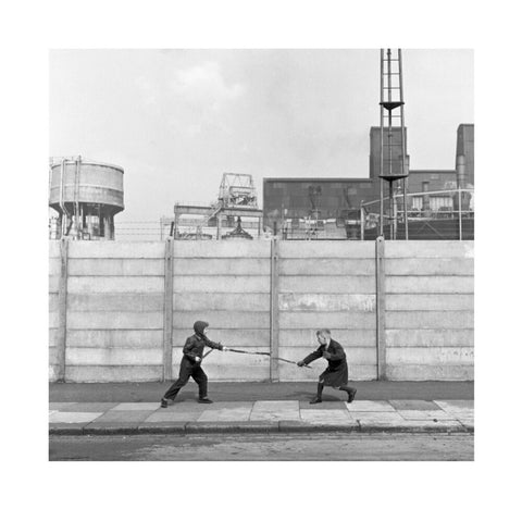 Two boys fighting with sticks in front of a concrete wall. c.1955