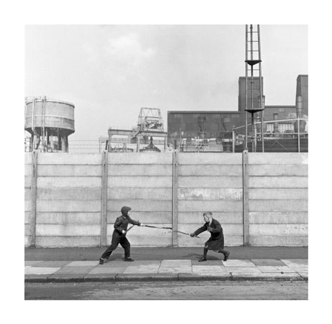 Two boys fighting with sticks in front of a concrete wall. c.1955