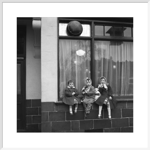 Three children perched on the windowsill of a pub. c.1955